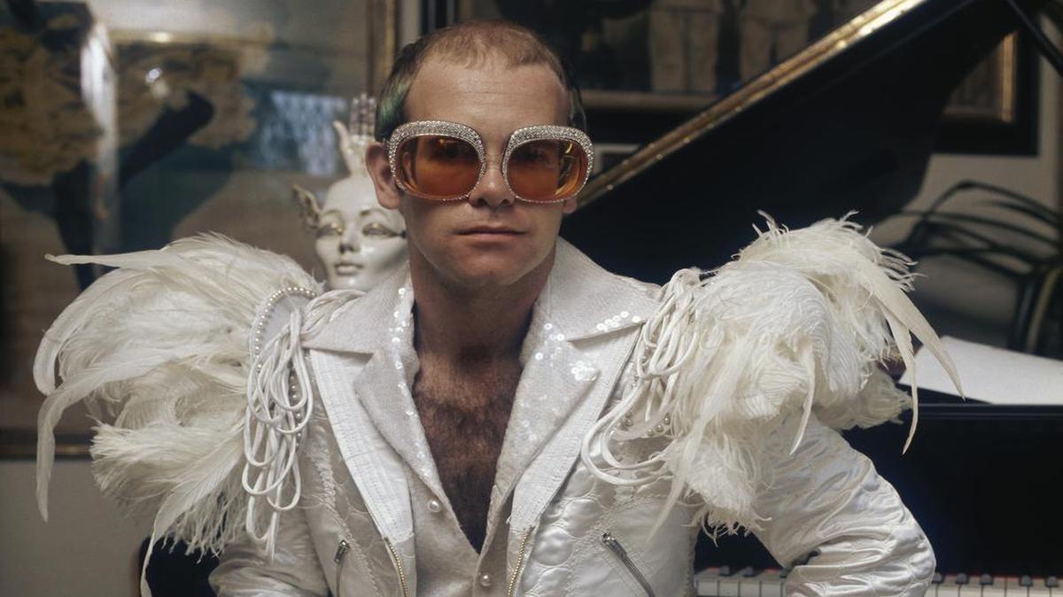English pop singer Elton John in a flamboyant stage outfit of white suit with feather trim and rhinestone encrusted glasses, circa 1973, in the “Goodbye Yellow Brick Road” and “Caribou” era.