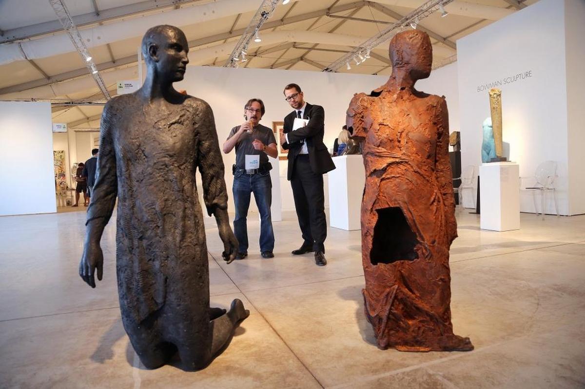 Art dealer Willoughby Garrish, center, takes a moment to answer questions regarding the pair of sculptures, “Melancholia,” on Tuesday, Dec. 5, 2017. Art Miami opened its doors at its new bayside location at the former Miami Herald building to kick off Miami Art Week and Art Basel Miami Beach.