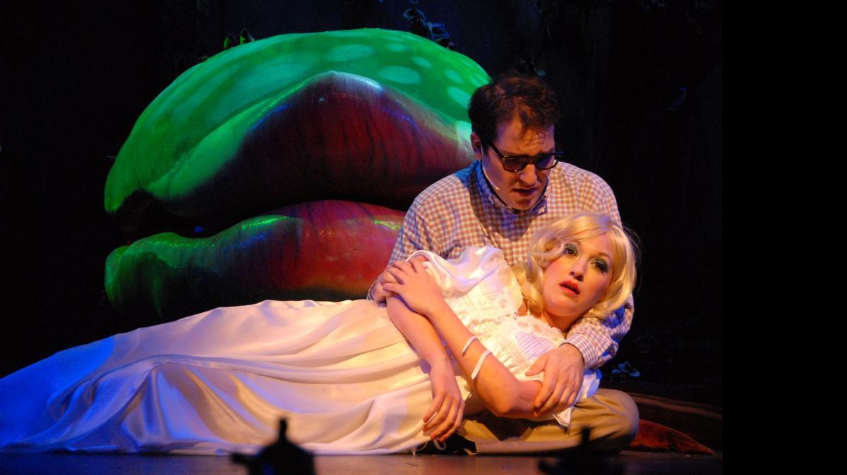 
Mike Westrich as Seymour comforts a pained Amy Miller Brennan as Audrey, while her namesake plant drools in Slow Burn Theatre’s ‘Little Shop of Horrors.’

