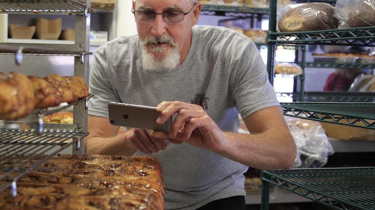Thomas Blocher takes pictures with his cell phone of his cinnamon rolls so that they can be shared on social media as a means of connecting with customers and other potential kitchen collaborators.