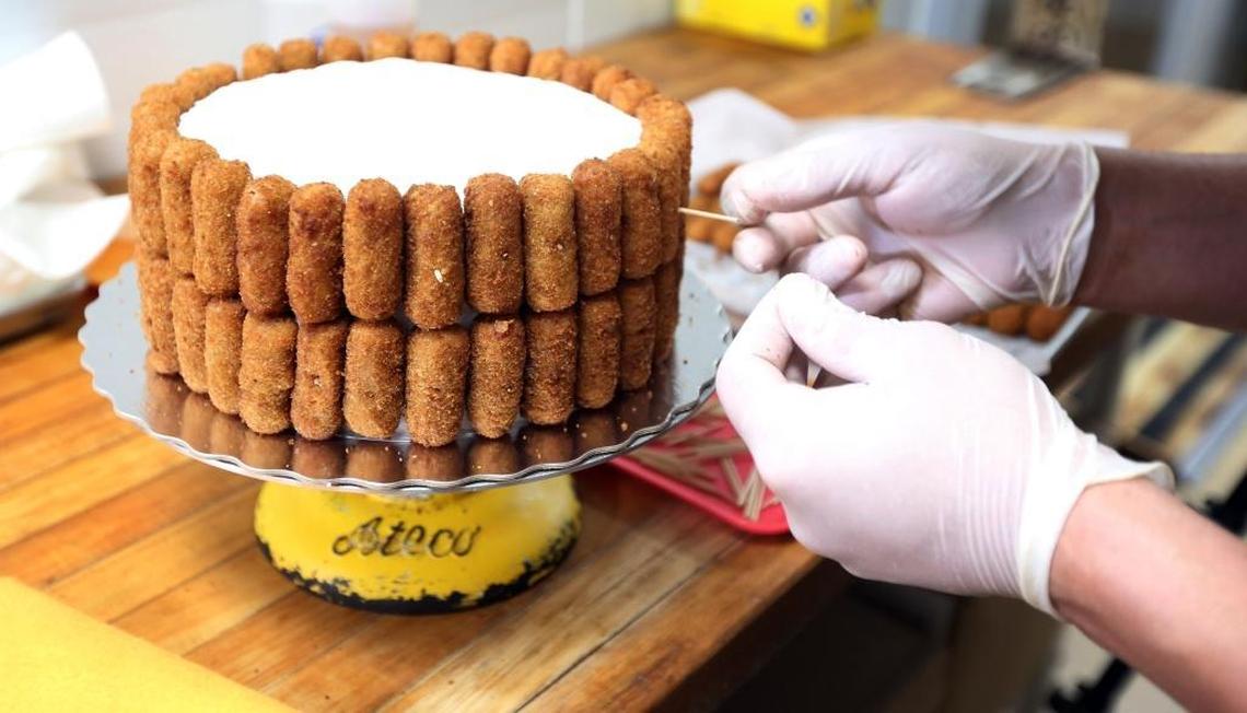 Maikel Rodriguez works patiently at building a croqueta cake masterpiece in the bakery at BreadMan Miami in Hialeah on Thursday, Feb. 15, 2018. Andy and Jessica Herrera, owners of Breadman Miami in Hialeah, call the cake ‘a marvel of engineering,’ as it is built using 100 croquetas and toothpicks, delicately stuck onto the outside of a vanilla cake with whipped icing and Nutella filling. (Other cake flavors and fillings are optional.) The price for the croqueta cake with Nutella filling is $56.99.