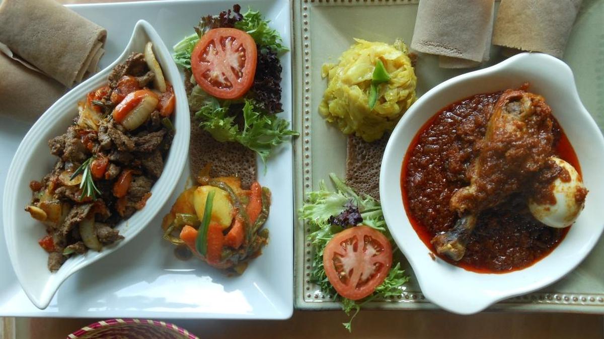 Siga tibs (sautéed beef) on the left with mixed vegetables and chicken doro wot with cabbage with injera flat bread.