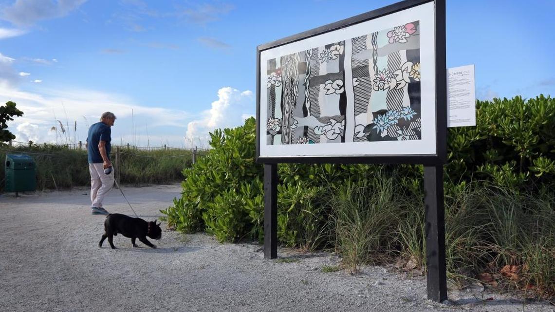 A man walks his dog Thursday near a replica of a piece of art, ‘Waterlilies with Willows,’ by Roy Lichtenstein, along Surfside beach’s walking path. The art is part of a program called Inside/Out, where replicas of some PAMM artworks are displayed outside.