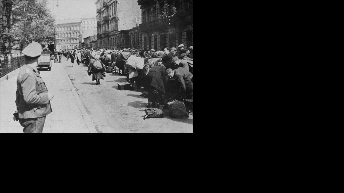 
GUARD DUTY: A Gestapo guard oversees a row of Jewish people who were lulled into a false sense of security. The Nazis created mock transit stations, complete with nonworking painted clocks, and posted time table schedules to give the impression that their Jewish victims were solely there for transport to colonies where they would be safe.
 This ruse maintained order.
Instead, an estimated 900,000 Jewish men, women and children were killed at Treblinka.Told they were in transit to a colony they were, instead, organized into lines that separated men and women, and were herded into gas chambers.
