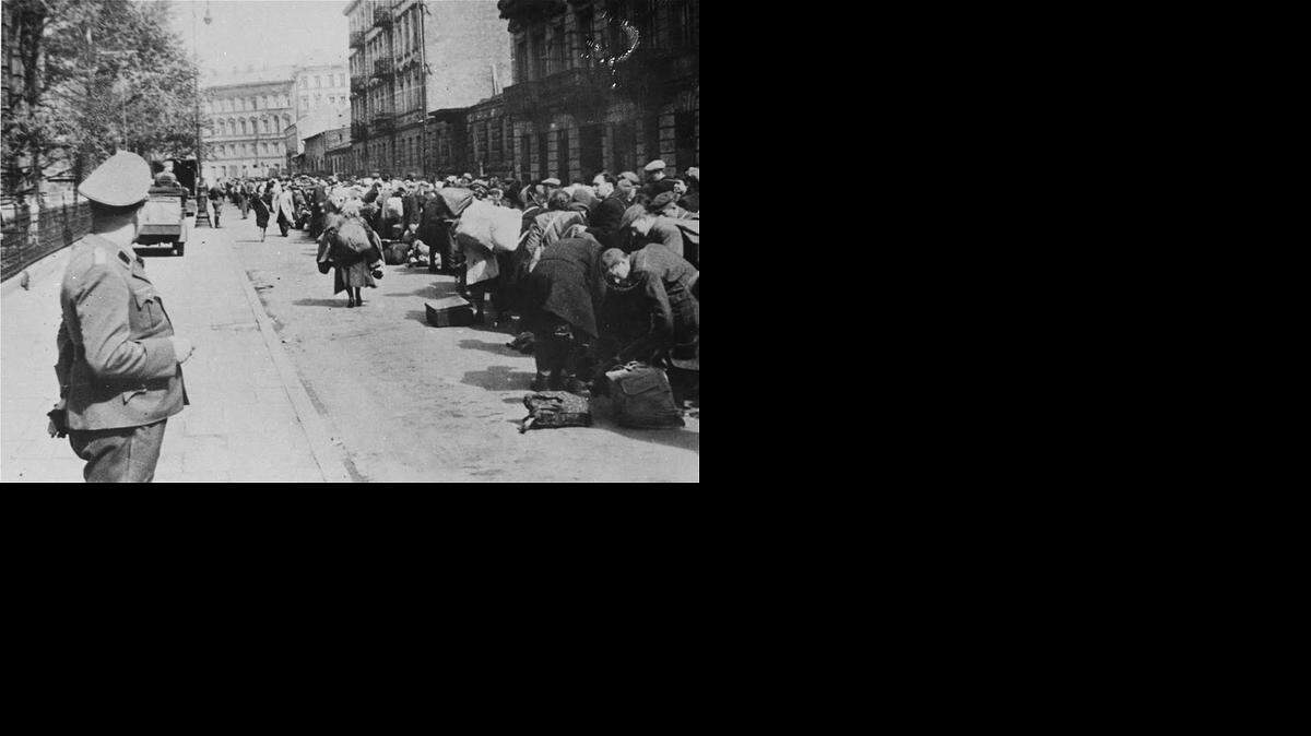 
GUARD DUTY: A Gestapo guard oversees a row of Jewish people who were lulled into a false sense of security. The Nazis created mock transit stations, complete with nonworking painted clocks, and posted time table schedules to give the impression that their Jewish victims were solely there for transport to colonies where they would be safe.
 This ruse maintained order.
Instead, an estimated 900,000 Jewish men, women and children were killed at Treblinka.Told they were in transit to a colony they were, instead, organized into lines that separated men and women, and were herded into gas chambers.
