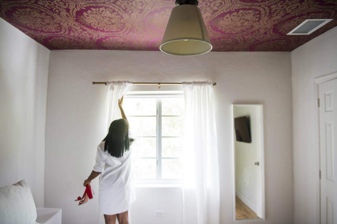 Jamila Ross opens a curtain in one of The Copper Door's guest rooms. Photograph by Felipe Cuevas. Hair and makeup by Latricia Russell for Makeup by RoryLee.