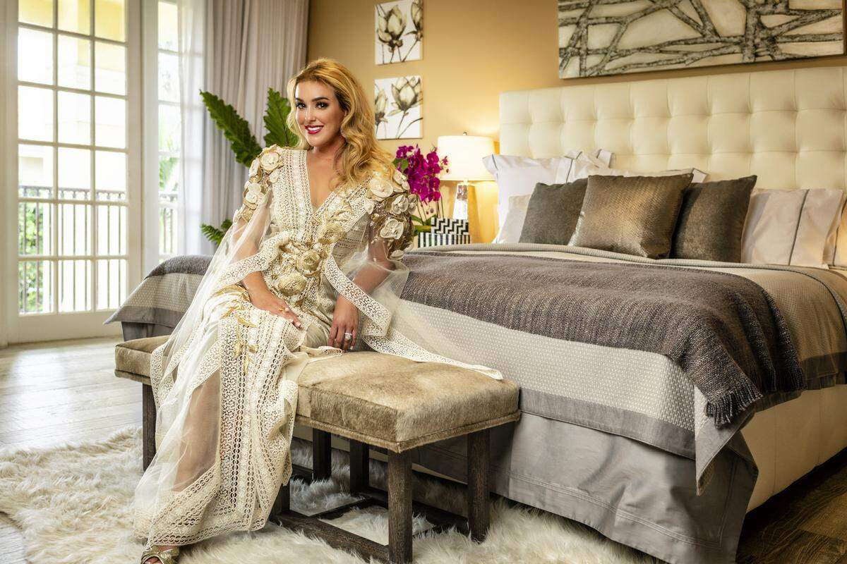 In the couple's master bedroom, Dr. Brianna Varas  wears a gown by Elie Youssef from Chernaya Bridal Design House; jewelry by Daniella Kronfle at Miami Design District. Bedding courtesy of ThreadCount. Photograph by Nick Garcia. Styling by Elysze Held. Hair and makeup by Pasquale Caselle and Yady Ochoa.
