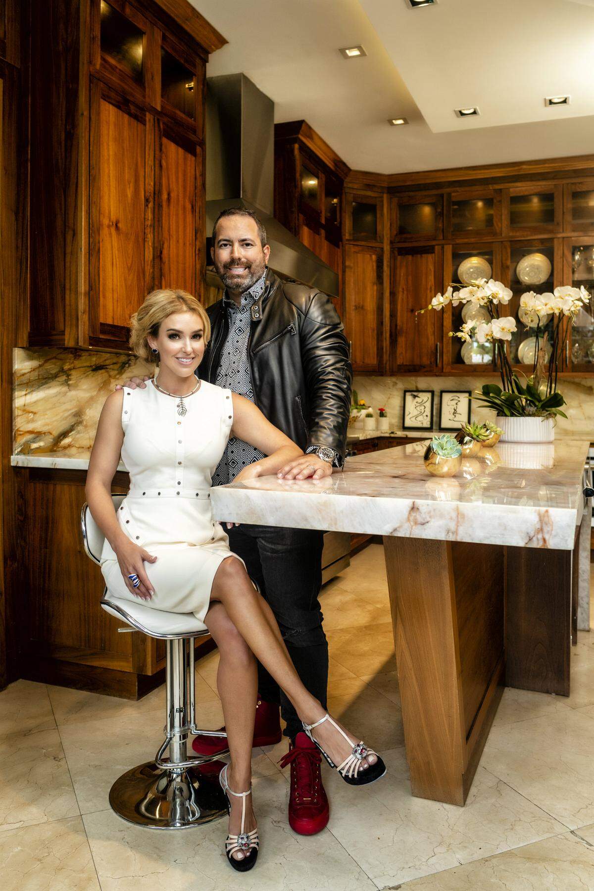 In their kitchen, Dr. Brianna Varas wears a top and skirt by Karolina Zmarlak; shoes by Gucci from Saks at Brickell City Centre; necklace by Chez Carole; earrings and ring by Daniella Kronfle at Miami Design District. Manny Varas wears a shirt by Versace; jacket by Ralph Lauren Black Label; and jeans by Vetements, all from Saks at Brickell City Centre; sneakers by Jimmy Choo. Photograph by Nick Garcia. Styling by Elysze Held. Hair and makeup by Pasquale Caselle and Yady Ochoa.