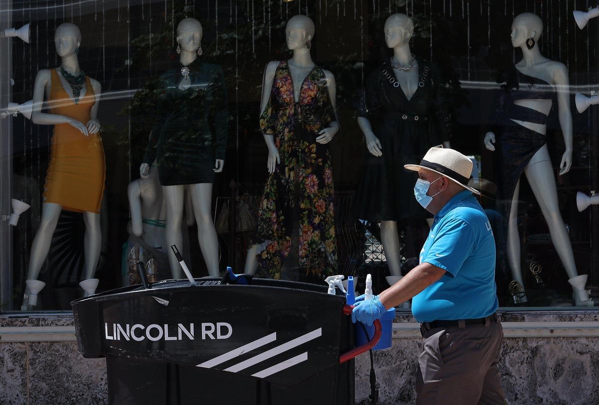 Lincoln Road Mall attendee walks the pathway cleaning and handing out masks to visitors on Lincoln Road on Wednesday, May 20, 2020.