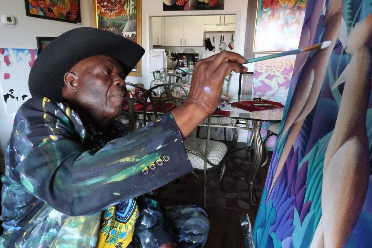 Louis Rosemond works on a painting inside his home in Opa Locka, Florida, on April 19, 2022. The Haitian-born artist lived in the Little Haiti neighborhood of Miami for 30 years, but was evicted in 2016 when his landlord sold the apartment building to developers who are preparing to build high-rise, high-priced condominiums on the property.