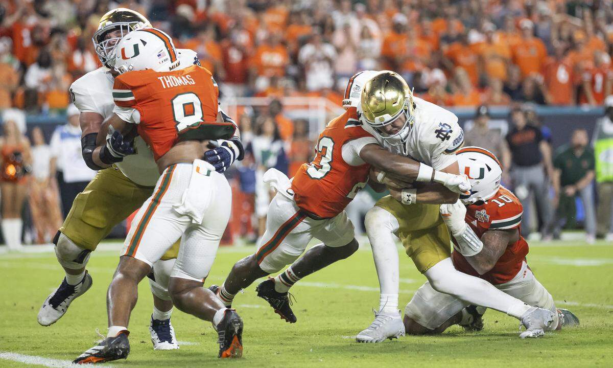 Miami Hurricanes defensive back Dylan Day (23) and linebacker Raul Aguirre Jr. (10) tackle Notre Dame Fighting Irish quarterback CJ Carr (13) in the second half of their NCAA football game at Hard Rock Stadium on Sunday, Aug. 31, 2025, in Miami Gardens, Fla.