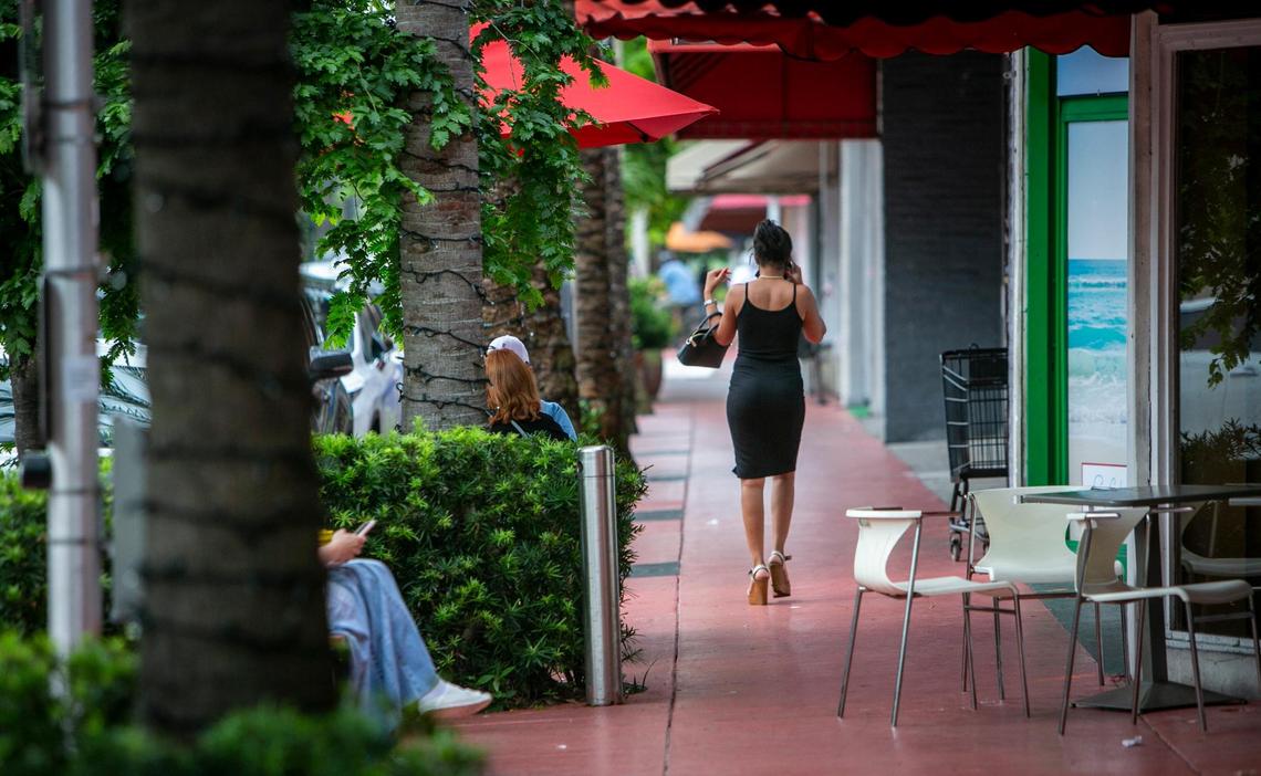 A lone woman walks past people sitting outside an ice cream shop in Surfside’s business district. Business owners here find their businesses struggling after the pandemic followed by the condo collapse.