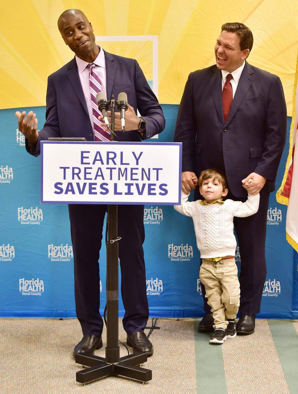 Florida Gov. Ron DeSantis with his son Mason listens as Dr. Joseph Ladapo, Florida surgeon general, addresses the media during a news conference in Jacksonville, Fla., on Tuesday, Jan. 4, 2022, to discuss COVID-19 testing policy and monoclonal antibody treatment availability in Florida. The event was relocated from the Department of Children and Families office building to the adjacent FDLE building after protesters, wanting to address the governor, refused to leave the initial news conference site. 