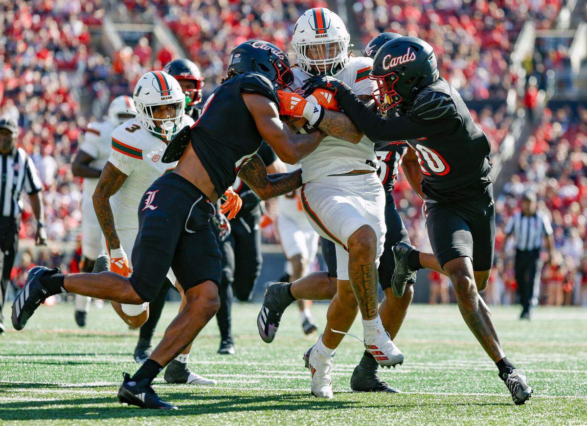 Miami Hurricanes running back Damien Martinez (6) breaks tackles by Louisville Cardinals defensive back Benjamin Perry (10) and defensive back Tayon Holloway (20) to score in the second half during an NCAA football game at L&N Federal Credit Union Stadium in Louisville, Kentucky on Saturday, October 19, 2024.
