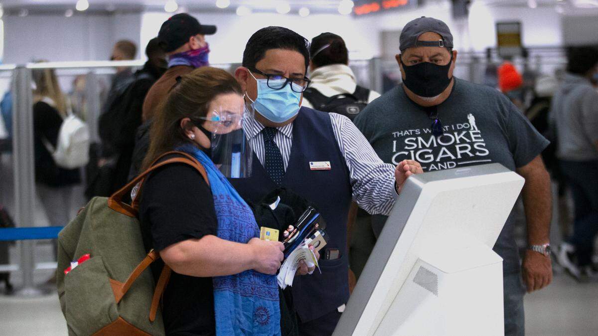 An American Airlines employee wears a mask while helping travelers to get their airplane tickets at Concourse D at the Miami International Airport on Monday, Dec. 28, 2020, in Miami, Florida. 