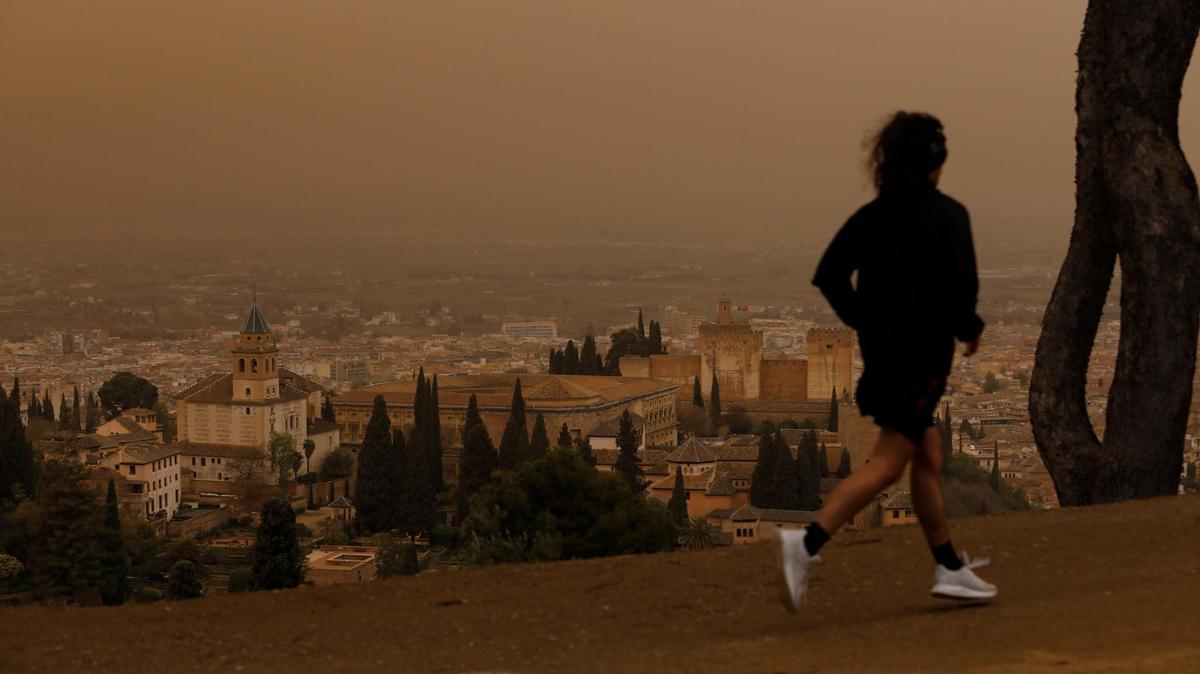 A man runs with a view of the Alhambra monument in Granada while the city is covered by a Saharan dust haze on March 24, 2022.