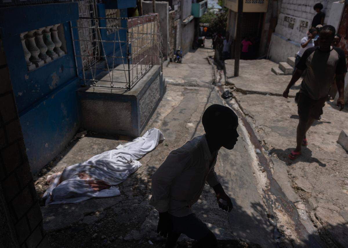 A dead body on the street covered in a shroud, as a child walks by. The man was coming to collect running water from a pump when police shot him for reasons that are unclear, according to family and witnesses.