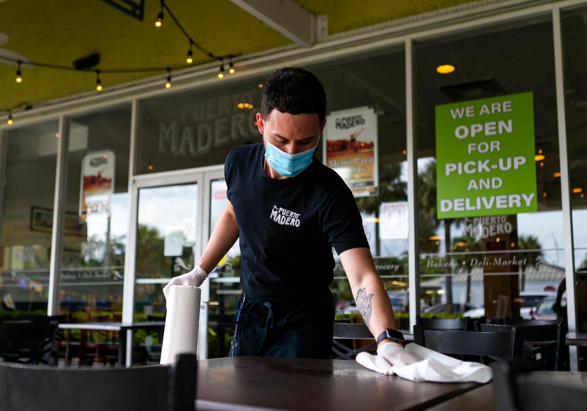 Juan Pablo Tarrago, 26, a waiter, cleans tables outside of Puerto Madero in Kendall on the first day Miami-Dade County allowed restaurants to reopen their dining rooms.