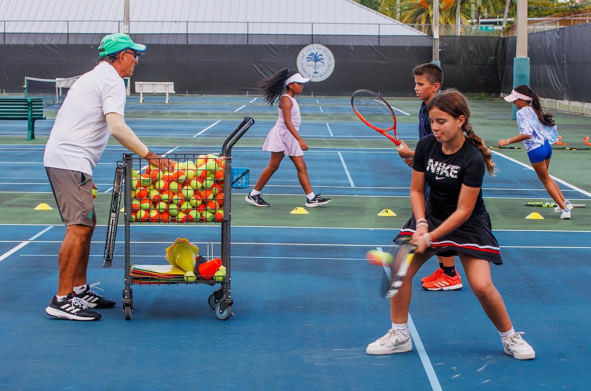 Coach Mario Osorio throws balls to students including Anais Soto during a session of the First Serve Miami Program at Moore Park in Miami, on Friday, October 06, 2023.