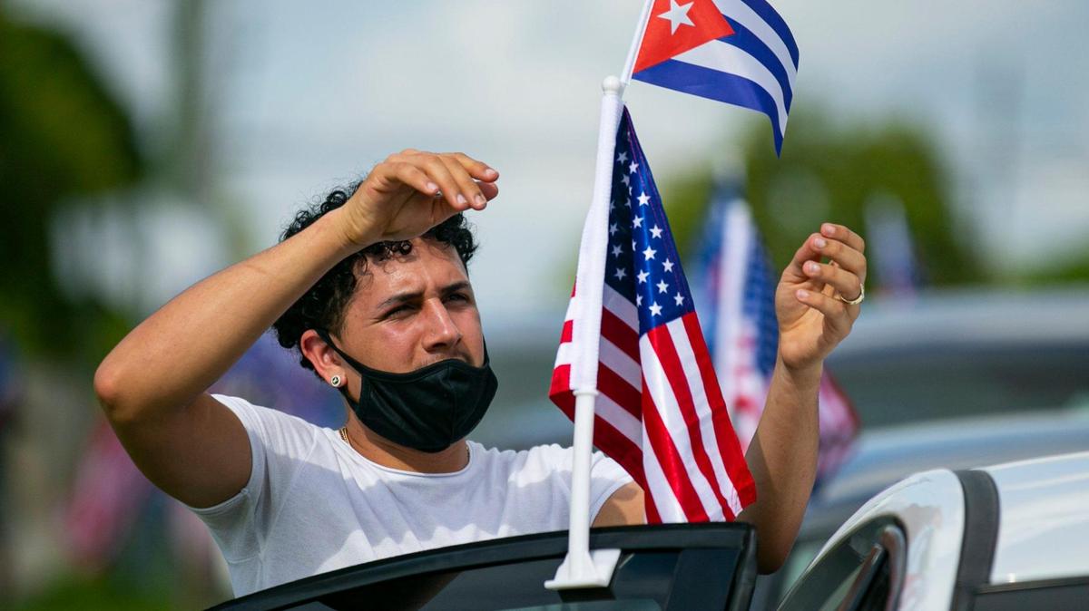 Yoandry Mora, 22, hangs flags from his car before the start of a Cubans Con Biden caravan at Bright Park in Hialeah, Florida on Saturday, September 19, 2020.