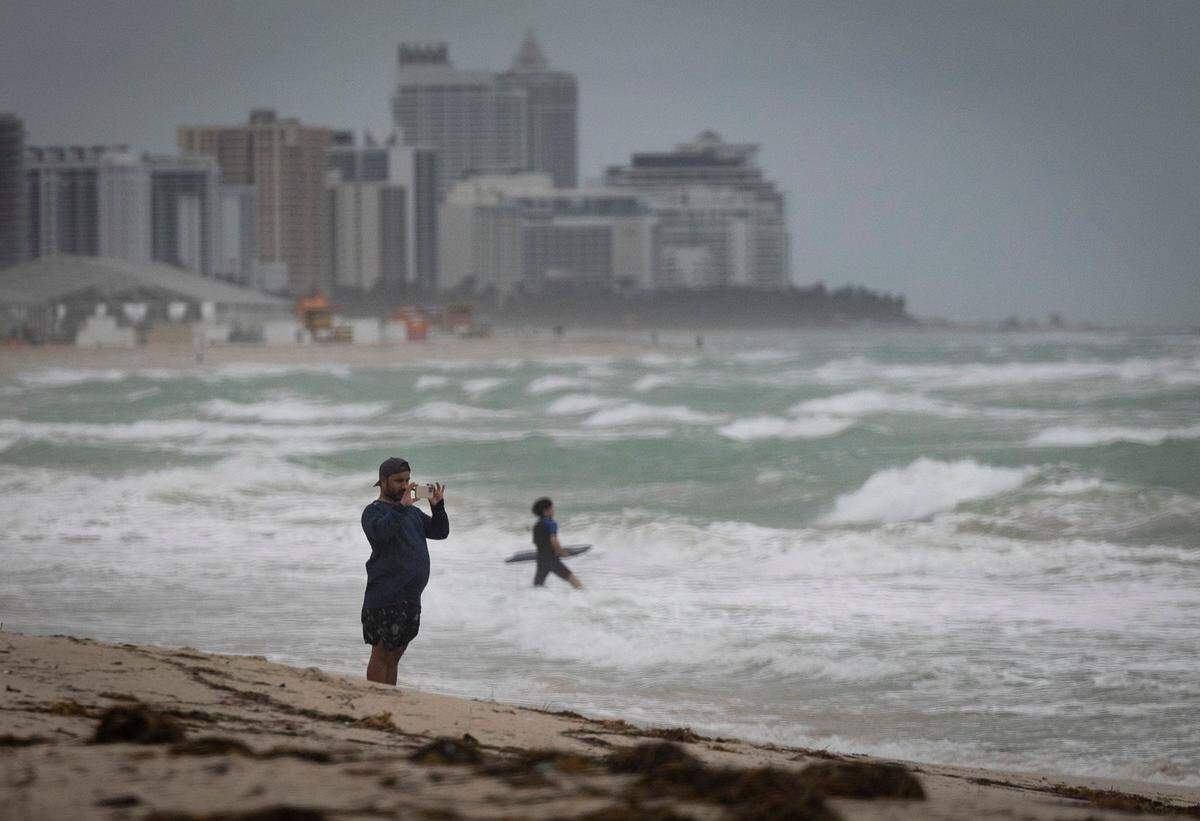 A man takes a photo of surfers and the waves during bad weather on Wednesday, Dec. 13, 2023, in South Miami Beach.