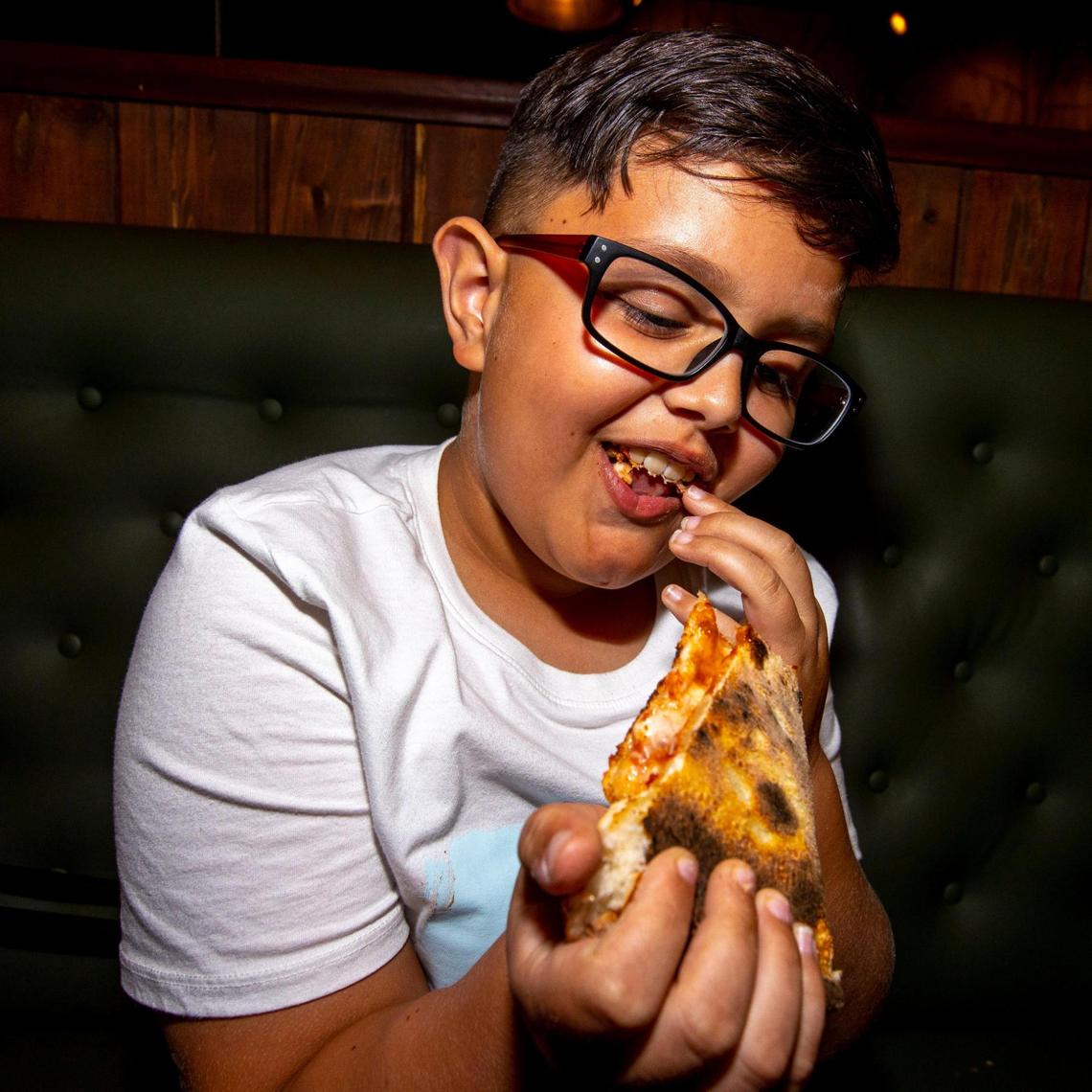 Youth food critic ‘Alexander the Great’ stuffs his mouth with a cheese pizza at Old Greg’s Pizza restaurant in Miami.