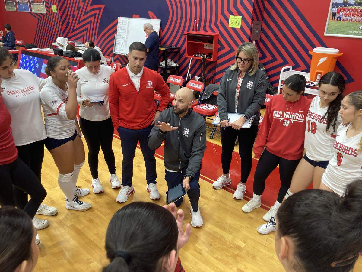Doral Academy girls’ volleyball coach Julio Arnaiz (middle) speaks to the Firebirds players during a timeout in Saturday’s Region 4-7A semifinal against Miami Palmetto at the Doral Academy gym.