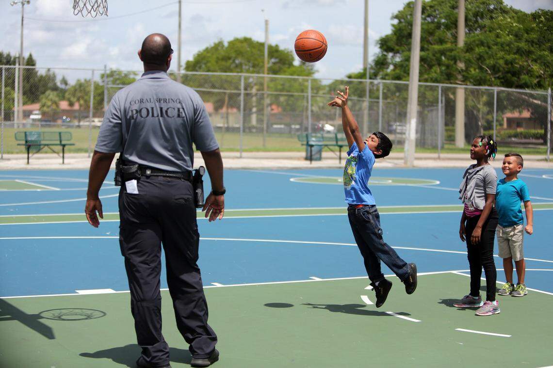 Coral Springs Police Officer Brian Gasper, a school resource officer at Coral Springs Charter School, watches as  Summer BreakSpot camper, Jayden Boodram, takes a basketball shot on Tuesday, July 19, 2016, as fellow campers, Tanisha Delva and Anthony Conteras look on.