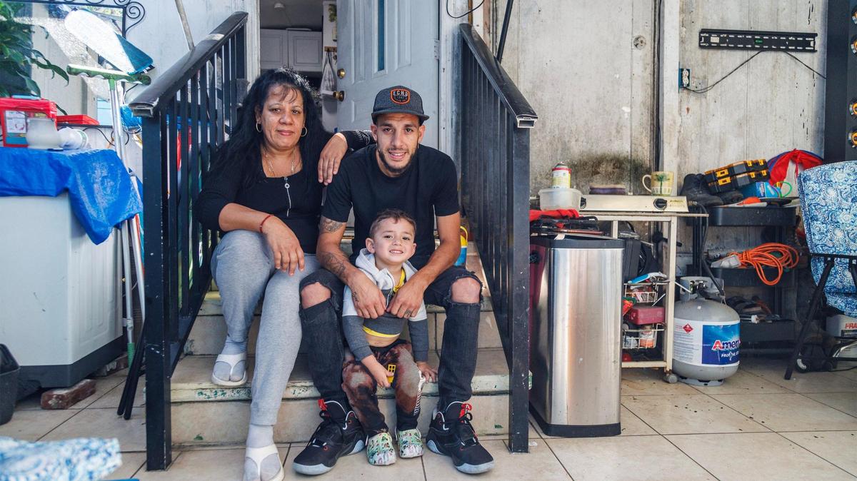Gloria Pérez está sentada con su hijo Danny Pérez y su nieto Caleb delante de su casa móvil, una de las cerca de 90 en el Gables Trailer Park, frente a Graceland Memorial Park North, en SW 44 Avenue, el 18 de octubre de 2023.