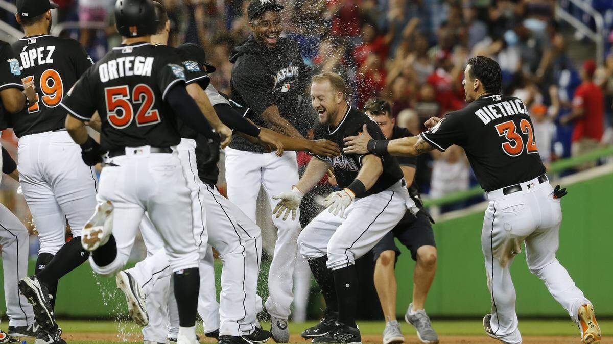 Miami Marlins pinch hitter Bryan Holaday, second from right, is rushed by teammates after his 11th inning winning RBI-single to defeat the New York Mets in a baseball game in Miami, Saturday, Aug. 11, 2018. (AP Photo/Joe Skipper)