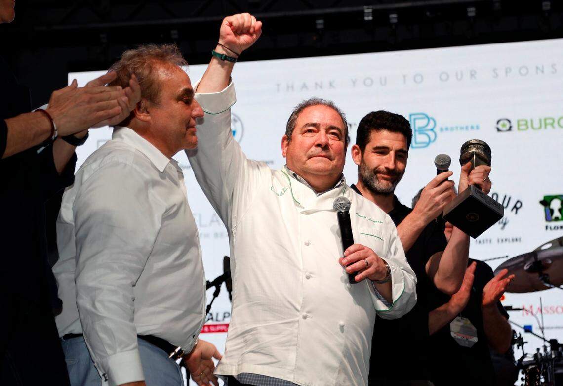 American celebrity chef, restaurateur, and television personality, Emeril Lagasse reacts as he is presented by South Beach Wine & Food Festival Founder Lee Schrager at left, and the Burger Bash event manager Randy Fisher, at right during the Burger Bash at the South Beach Wine & Food Festival on the sand by the Ritz Carlton in Miami Beach, Florida on Feb. 23, 2023.