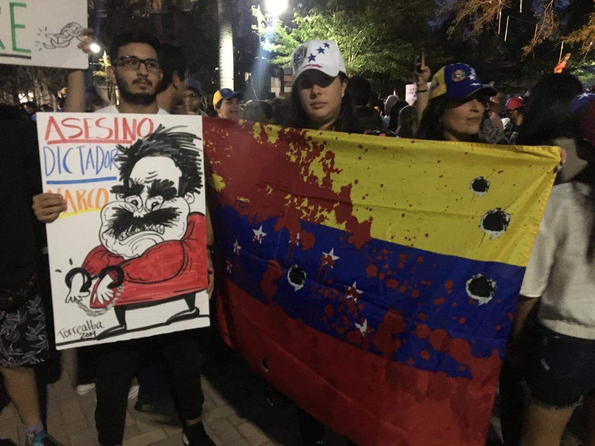Protester Sabina Contreras, right, holds up a Venezuelan flag modified to appear bloodstained and covered in bullet holes during a large rally in downtown Doral on Wednesday night to call for the ouster of President Nicolás Maduro. Opposition leader and National Assembly President Juan Guaidó declared himself the interim president on Wednesday and called for new elections.