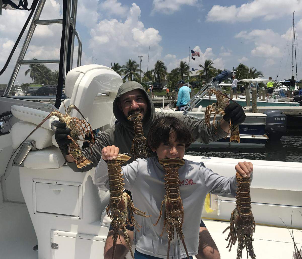 Sebastian Suarez, 9, of Cutler Bay, and Dennis Perez, 39, of Orlando, pose on a boat at Black Point Marina in South Miami-Dade County with lobster they caught Wednesday, July 24, 2019, opening day of lobster mini season.