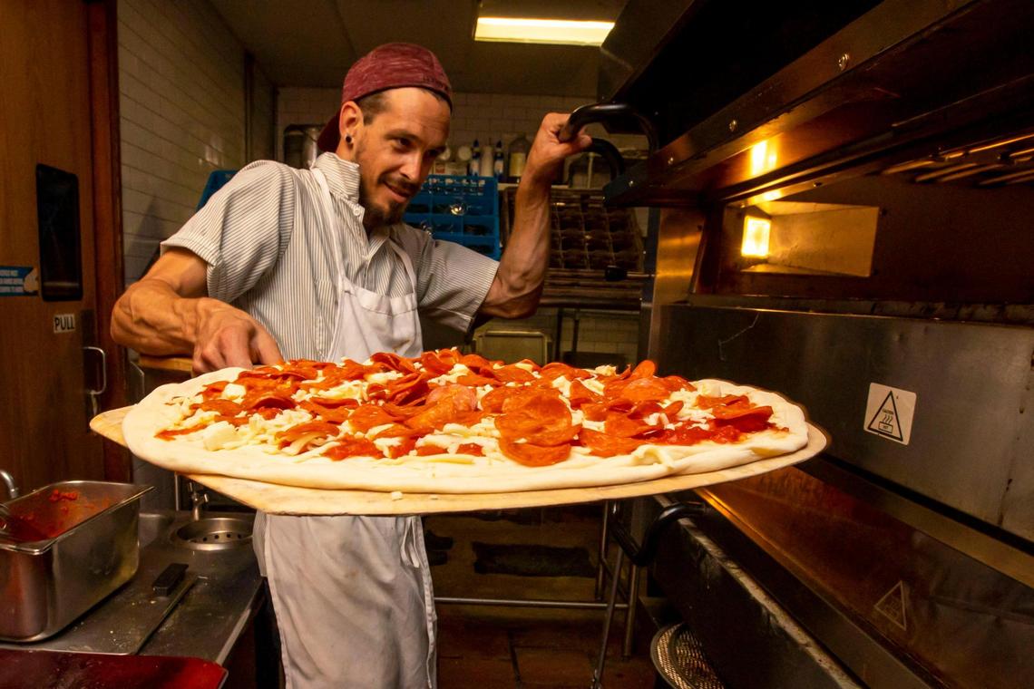 Pizzaiolo Eddie Zinkand sets a pizza inside the oven at Old Greg’s Pizza restaurant in Miami.