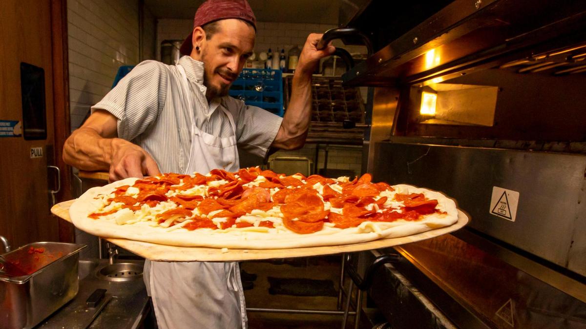 Pizzaiolo Eddie Zinkand sets a pizza inside the oven for baking at Old Greg’s Pizza restaurant in Midtown.