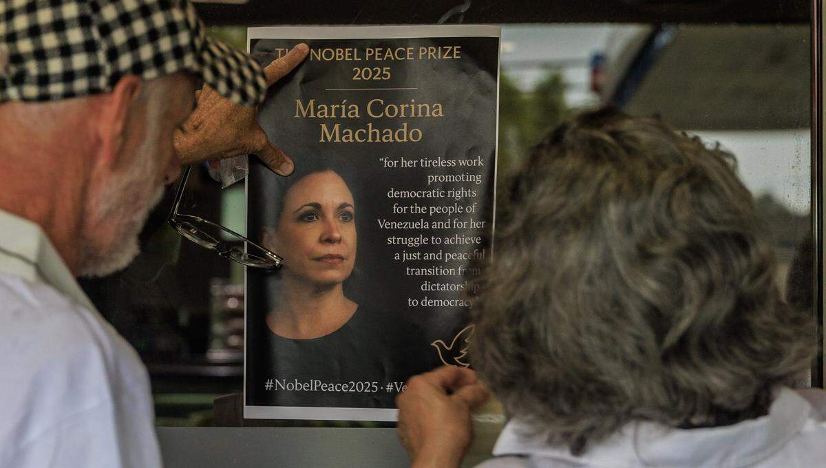 Jose Vanegas (left) helps Iris Wilthew, a Venezuelan resident of Coral Gables to place a poster she printed with the announcement of the Nobel Peace Prize award given to Venezuelan opposition leader María Corina Machado, in the window at El Arepazo Restaurant in Doral, on Friday October, 10 2025.