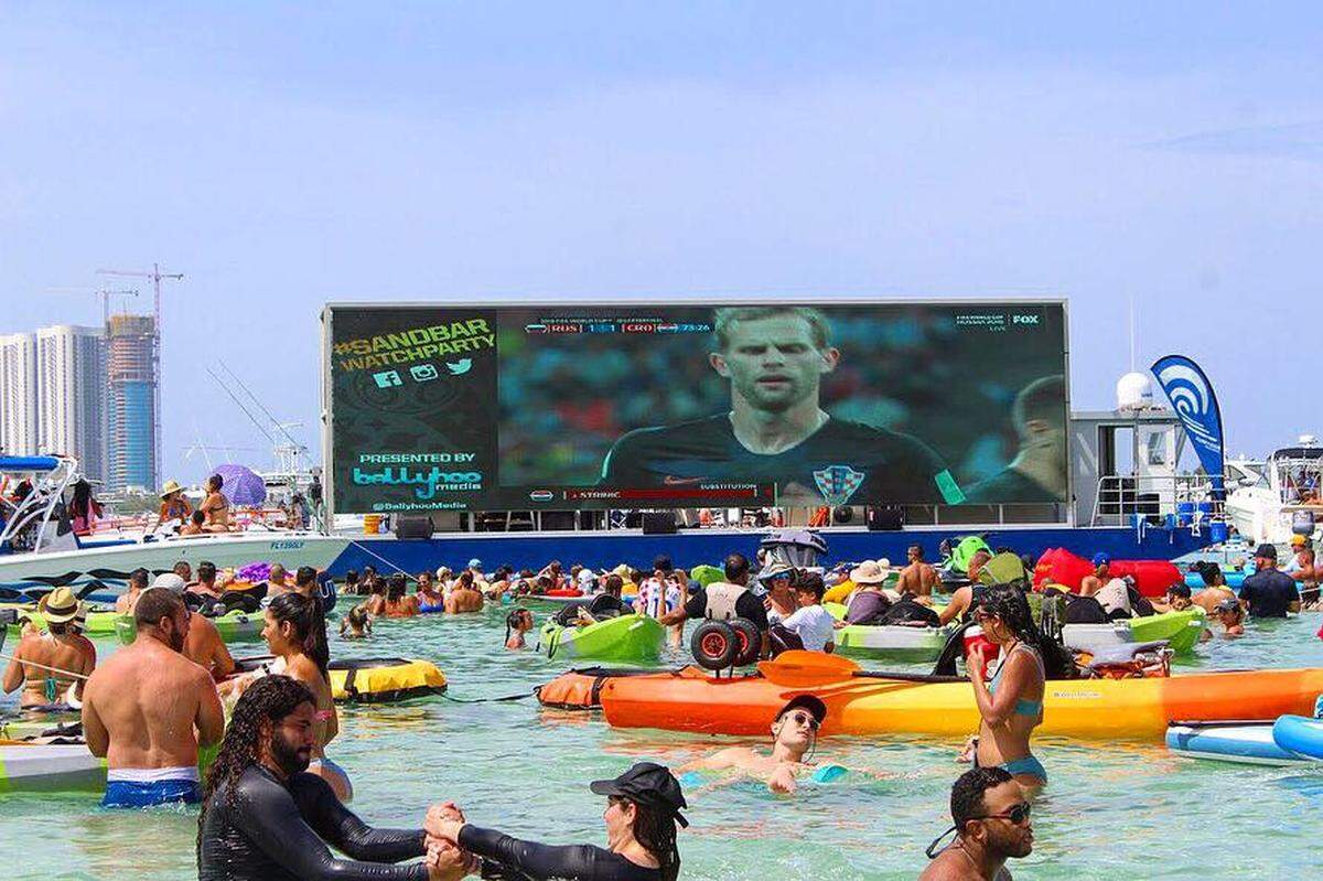A billboard barge with a giant screen shows a 2018 World Cup soccer game at Haulover Beach.