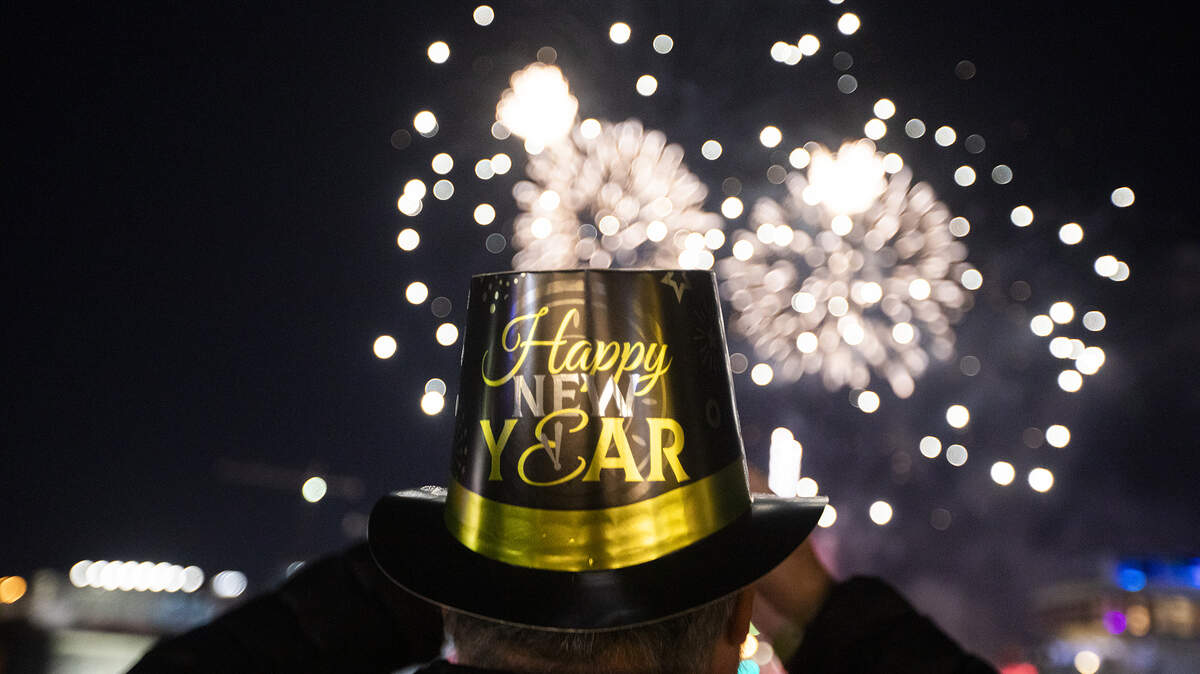 A person wearing a Happy New Year hat watches fireworks over Biscayne Bay during New Year’s Eve celebrations as crowds gather to welcome 2026 at Bayfront Park on Dec. 31, 2025, in Miami.