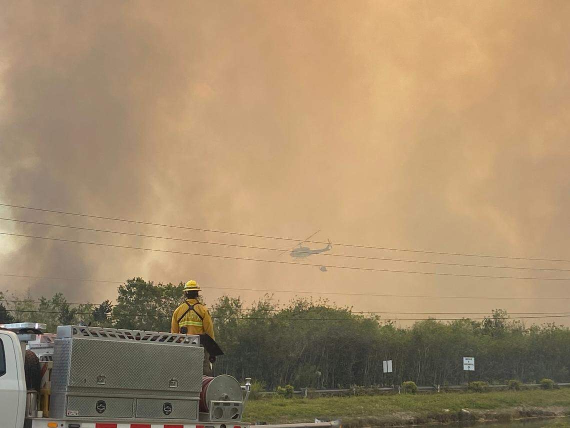 A helicopter pours water over the brush fire around Southwest 344th Street and 117th Avenue in Homestead on Thursday afternoon, March 20, 2025. The brush fire had started around Card Sound Road near Florida City but by Thursday, the fire had spread to Homestead. Authorities said the fire was burning 22,000 acres of brush — with 22% containment.