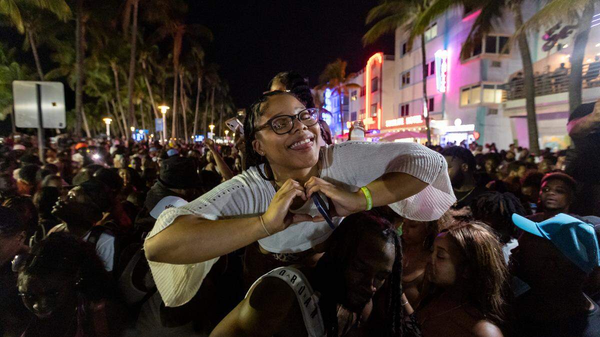 A woman makes a heart with her hand in a large crowd on Ocean Drive during spring break on Saturday, March 11, 2023, in Miami Beach, Fla.