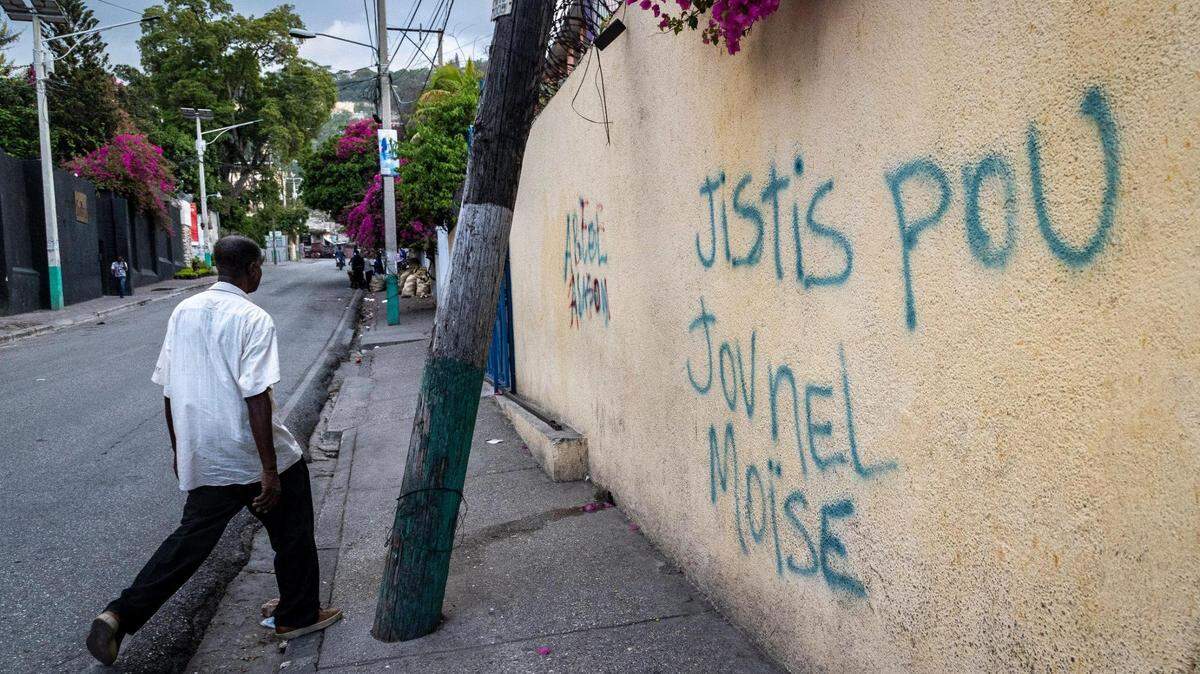 A man walks by graffiti on a wall demanding justice for slain Haitian President Jovenel Moïse in Pétionville. The trial of four South Florida defendants will begin Monday, March 9, 2026.