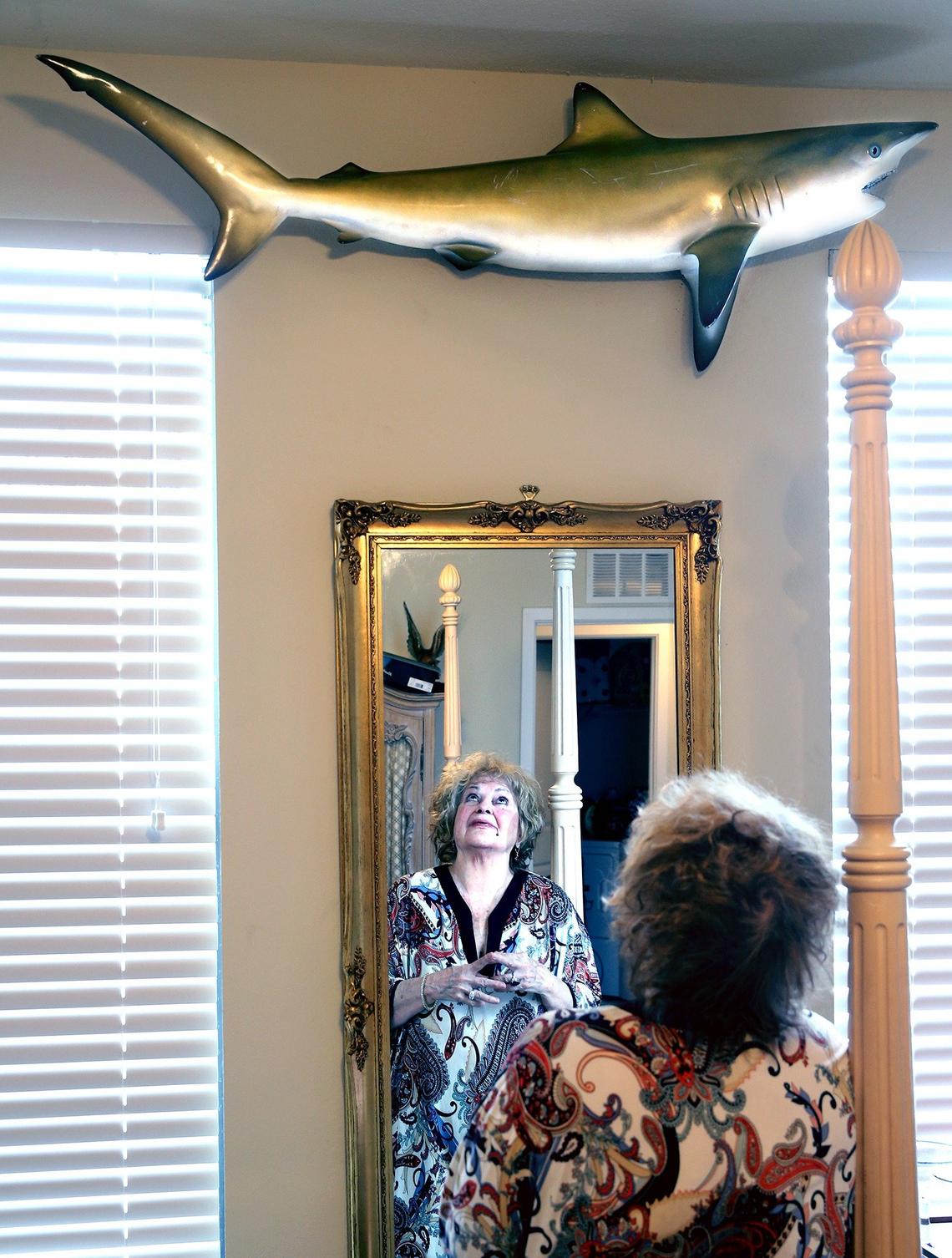 Elaine Shure, 80, studies Oscar the shark, hanging above, in her Boynton Beach apartment. The crew told her it was a rare Golden Shark. It’s not, but she still treasures the fish.