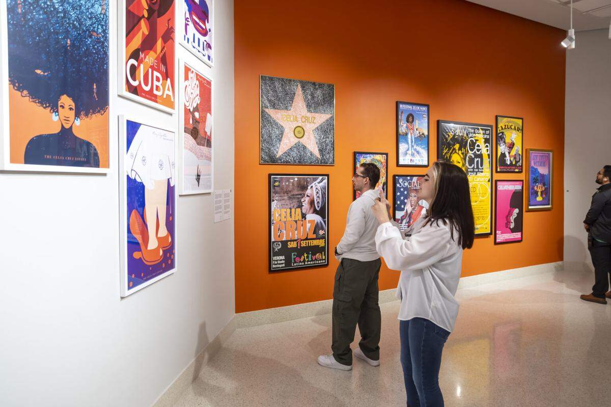 Visitors to MDC’s Hialeah Art Gallery look at an array of posters celebrating Celia Cruz’s concerts, collaborations, and a documentary film about her life.