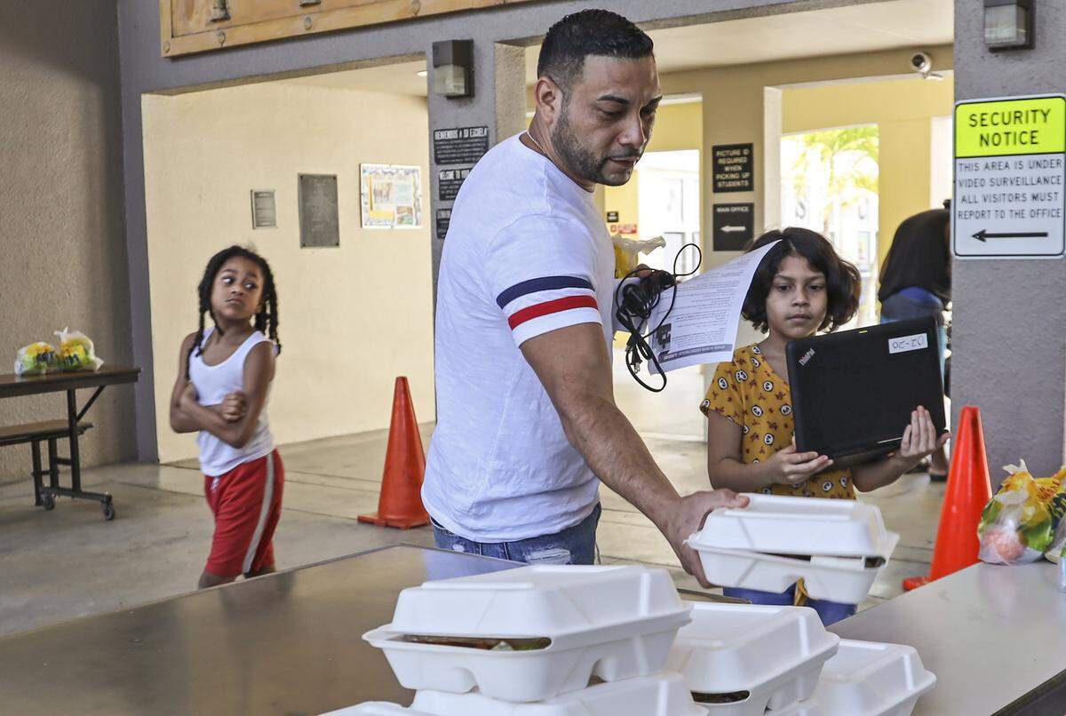 Nelson Navas, center, grabs lunch for his daughter, Deliylah Navas, 8, right, at Toussaint L’Ouverture Elementary School in Miami’s Little Haiti neighborhood. The school is serving free meals (breakfast and lunch) during the coronavirus pandemic. Families can pick up meals from 4 to 5:30 p.m. on Tuesdays and Thursdays.