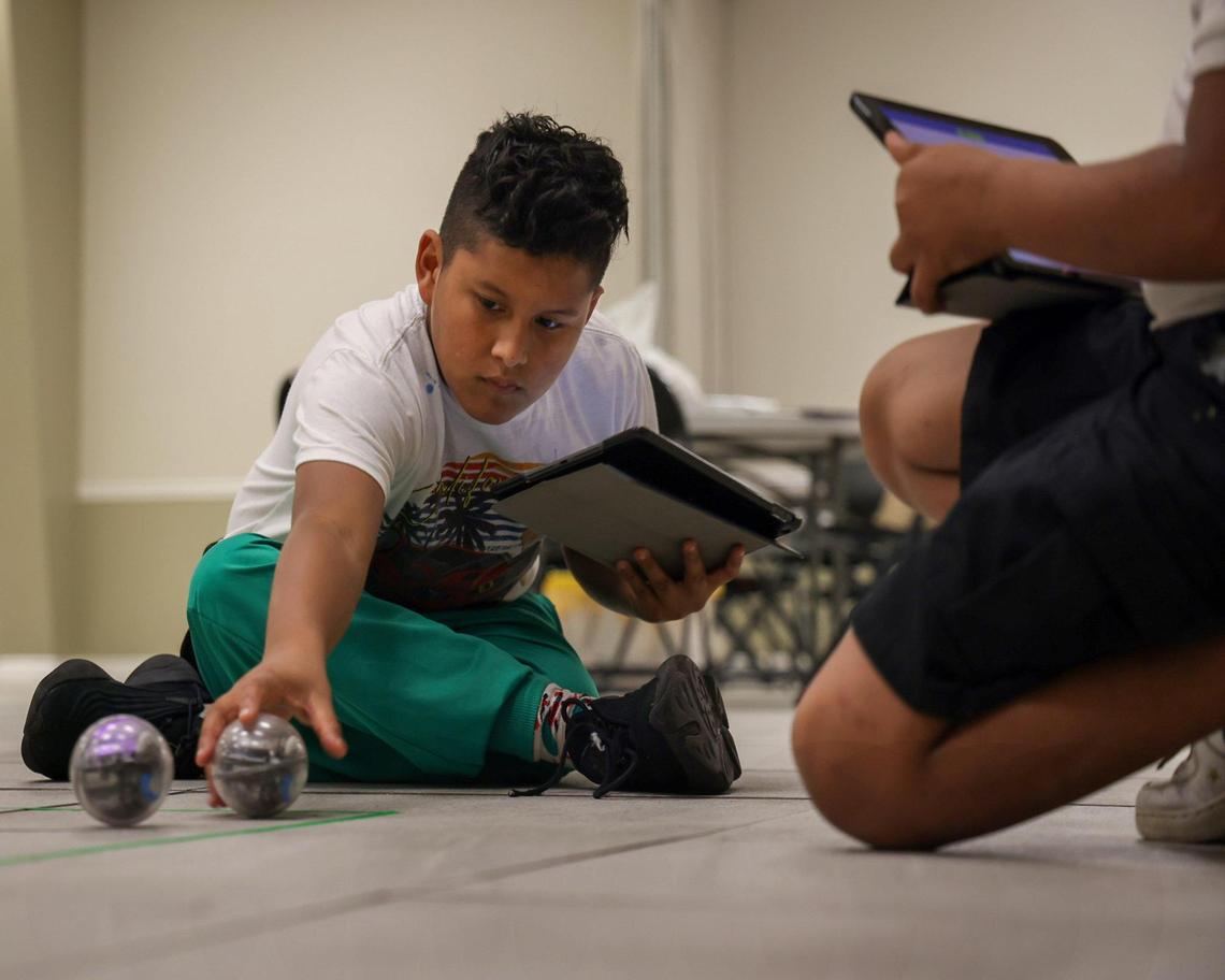 Fourth grader Fernando Gallo, 12, left, places the small robot on the floor while programming it to run a specific pattern as part of the Fab Lab launched at the Phichol Williams Community Center in Homestead, Florida on Wednesday, Jan. 17, 2024.