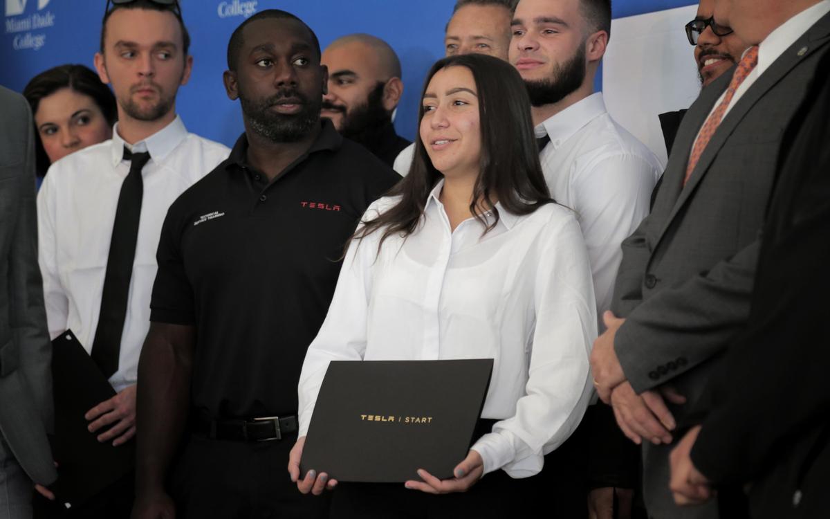 Miami, December 4, 2019- Diana Molero (center) poses for photos holding her diploma during a graduation ceremony at MDC’s West Campus. The nine students were the first to graduate with a Career Technical Certificate in Advanced Automotive Service Technology .Miami Dade Collegeâ€™s West Campus hosted an inauguration ceremony on Wednesday, Dec. 4, of its new, one-of-a-kind and state-of-the-art Electric Vehicle Training Center that will train students as Tesla technicians for the leader in electric car design and manufacturing. MDC is the first institution in the Southeastern United States to partner with Tesla to offer a certificate training program for service technicians called Tesla START. The Career Technical Certificate in Advanced Automotive Service Technology â€“ Tesla Technician Program powered by Tesla START is an accelerated 12-week program that pays students while they train to become an electric vehicle technician. Tesla provides the vehicles, equipment, instructor, tools and curriculum for hands-on learning. Following successful completion of the program, students are eligible to work as full-time employees at a Tesla service center.