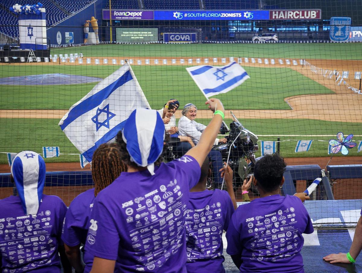 A motorcade cruises through third base, home plate and first base at loanDepot Park in Miami as children wave flags with cheers.