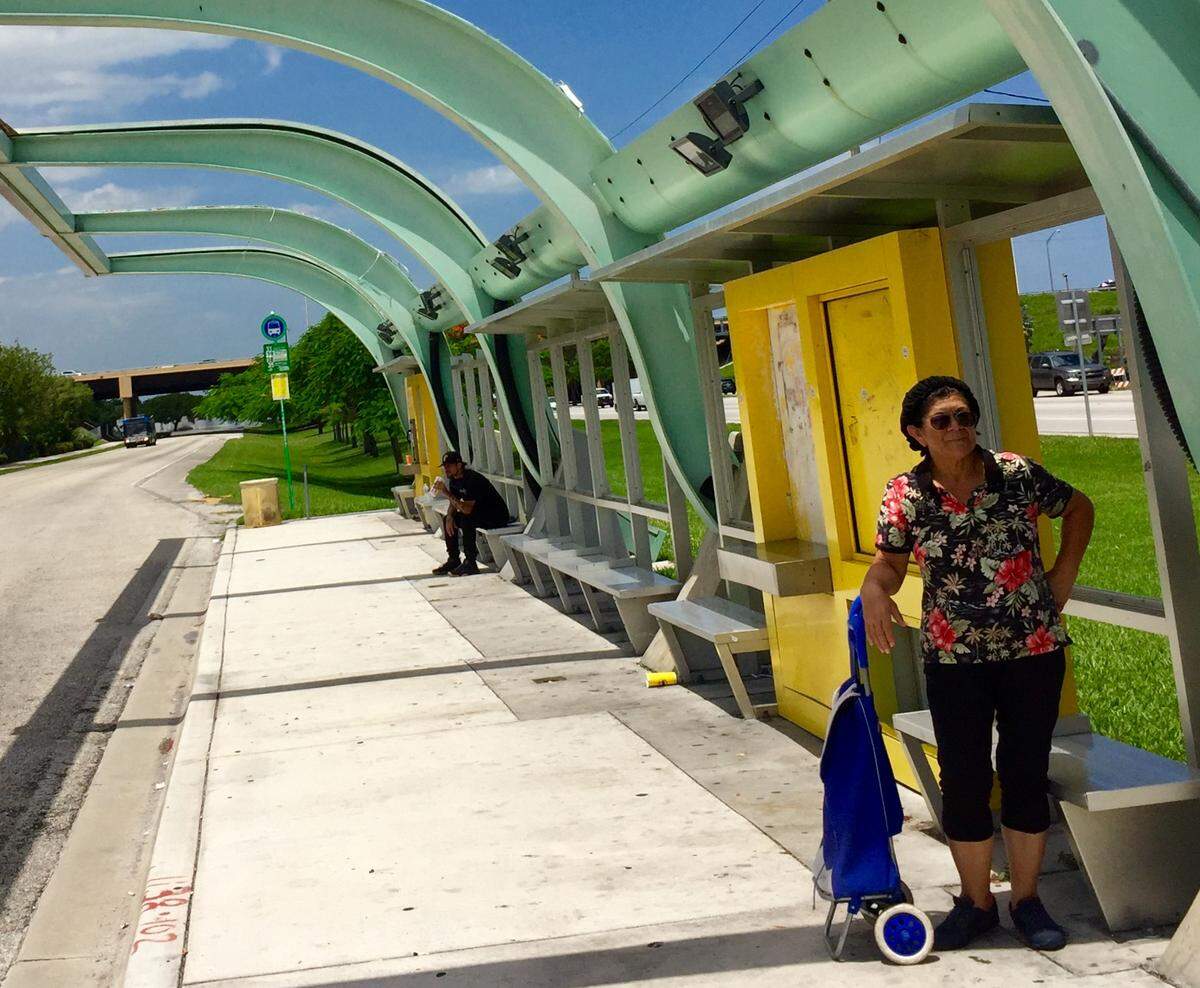 Elena Gregory waits for the bus in the only sliver of shade she can find.