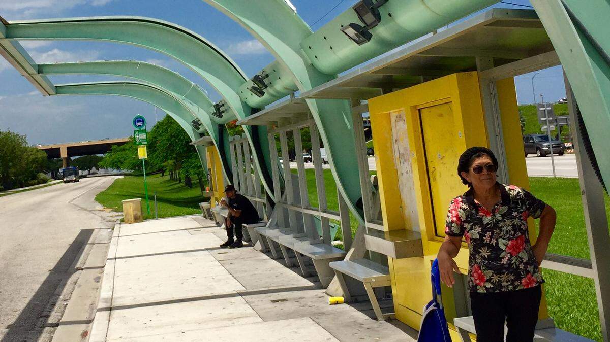 Elena Gregory waits for the bus in the only sliver of shade she can find.