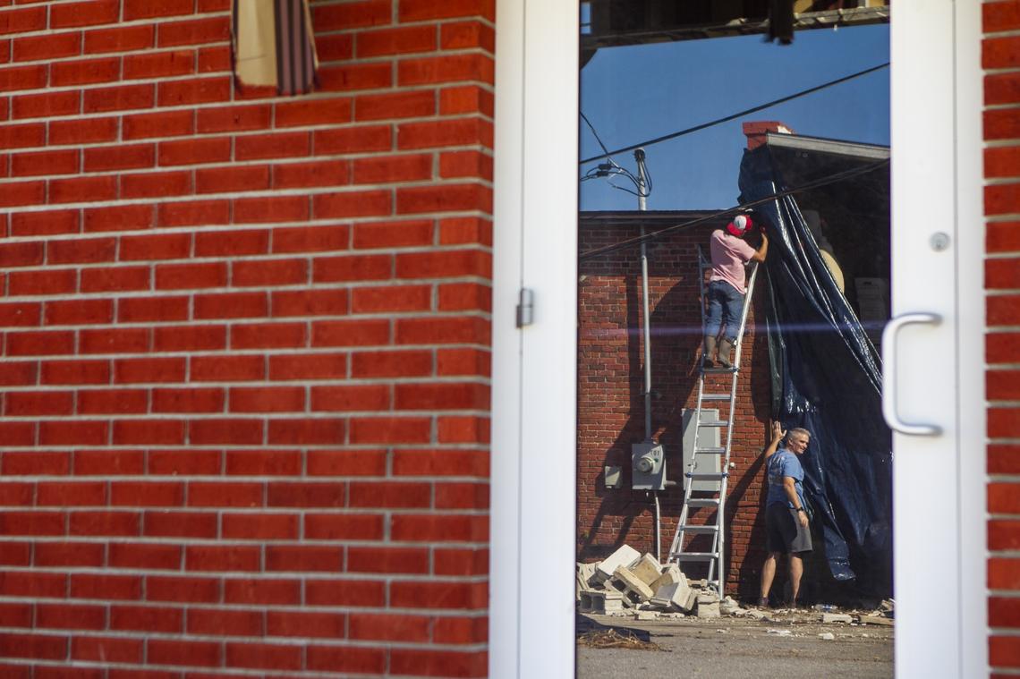 Rick Taylor, bottom, and his nephew, Marcel Duarte, work to patch their warehouse with a blue tarp in Port Saint Joe, Florida eight days after Hurricane Michael devastated the area leaving hundreds of thousands without shelter, power and food.